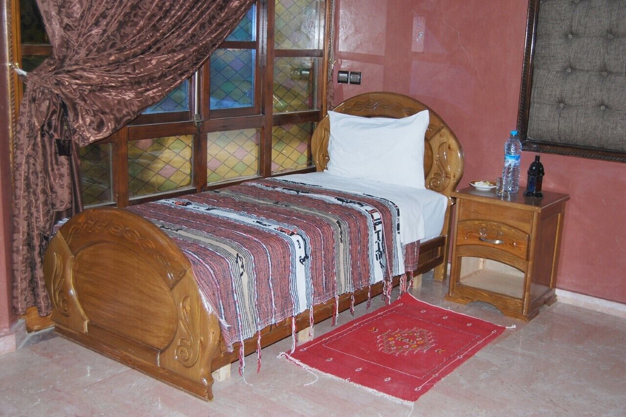 A room with a wooden bed, a nightstand, a red rug, and a window with curtains.