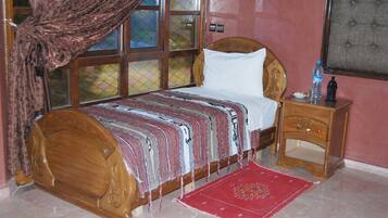 A room with a wooden bed, a nightstand, a red rug, and a window with curtains.