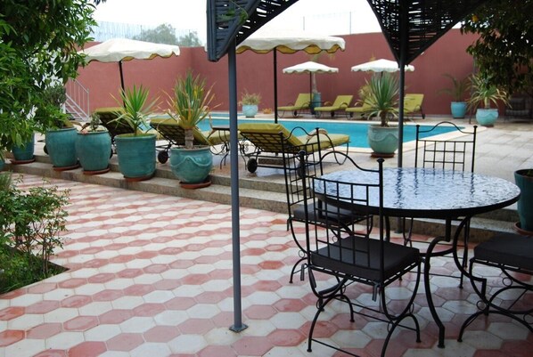 A poolside area with hexagonal tiled flooring, a round metal table with four chairs, and several potted plants and umbrellas. - Riad les jardins Mabrouk (Taroudant)