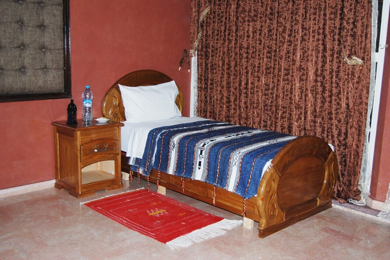 A bedroom with a wooden bed, a nightstand, a red rug, and a patterned curtain.
