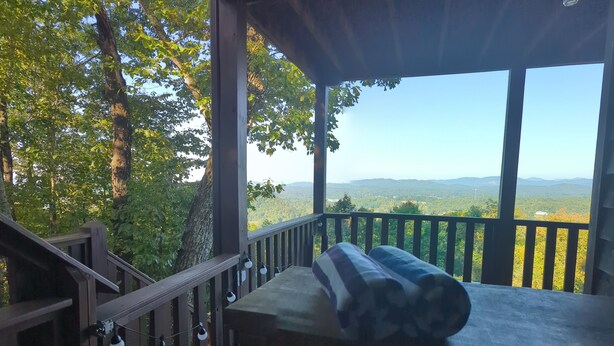 Um deck de madeira com guarda-corpo, um banco e vista para uma paisagem arborizada.