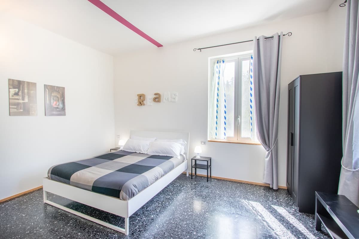 Un dormitorio con cama, mesita de noche, televisor y ventana con cortinas.