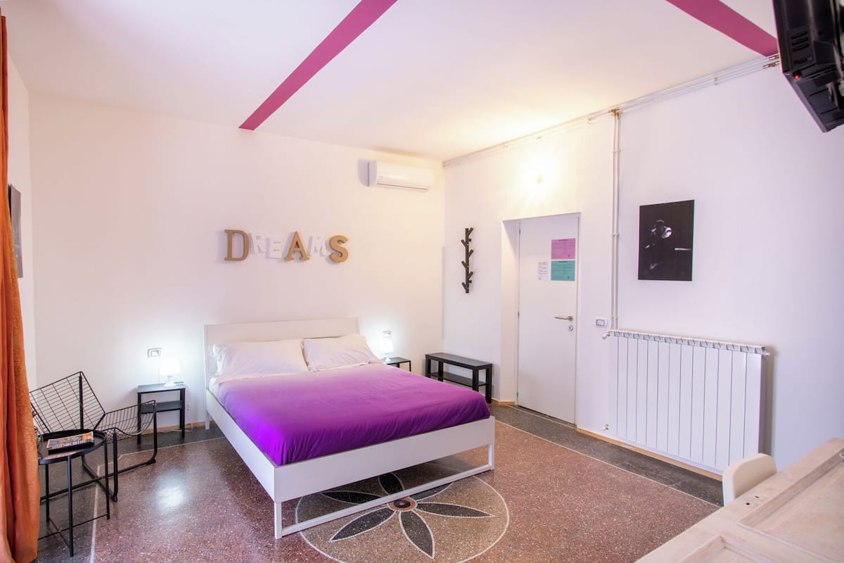 Un dormitorio con cama, dos mesitas de noche, un radiador, una puerta con un aviso y una obra de arte colgada en la pared.