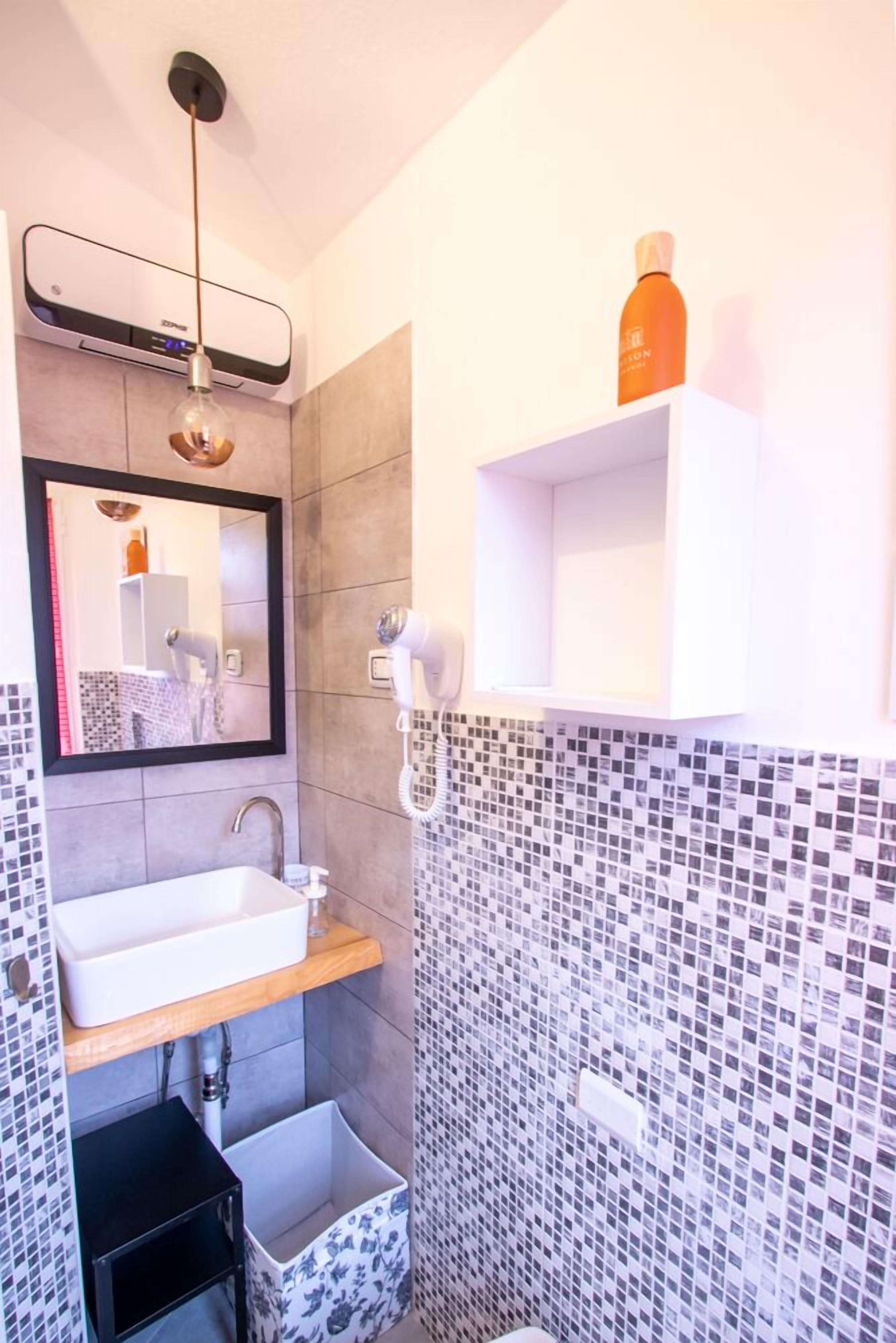 Une salle de bain moderne avec un grand miroir, un lavabo, un sèche-cheveux et un mur recouvert de carreaux.