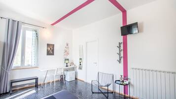 A modern room with a white desk, a chair, a small table with a radio, a TV mounted on the wall, and a radiator.