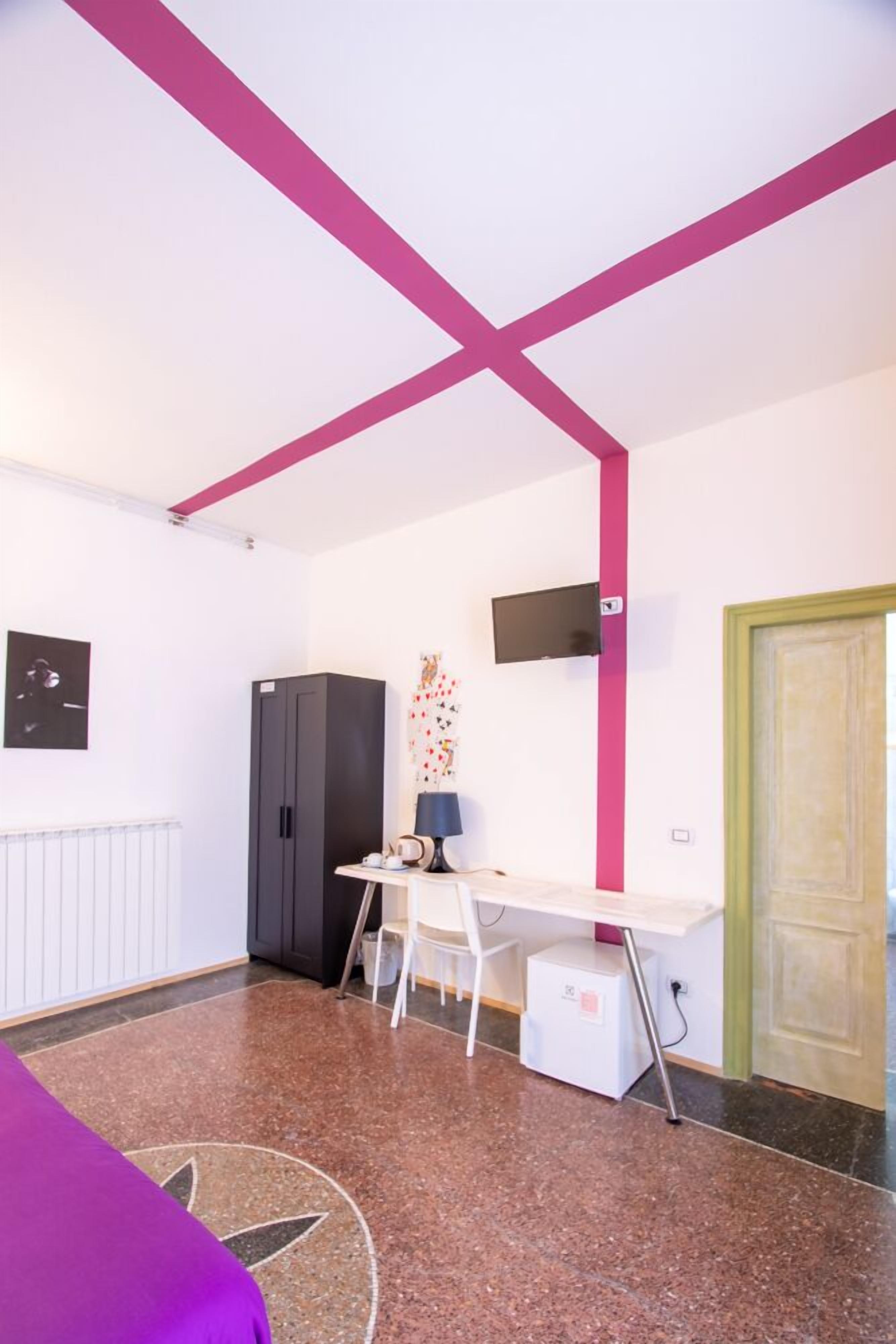 A room with a white ceiling, a black wardrobe, a desk with a chair, a television on the wall, and a green door.