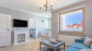 Een moderne woonkamer met een televisie, open haard en groot raam met uitzicht over de stad.