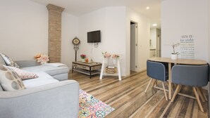 A modern living room with a grey sofa, a wooden coffee table, and a dining area with a small table and two chairs.
