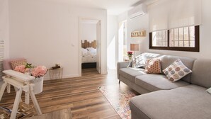 A modern living room with a grey sofa, wooden flooring, and a small table with flowers.