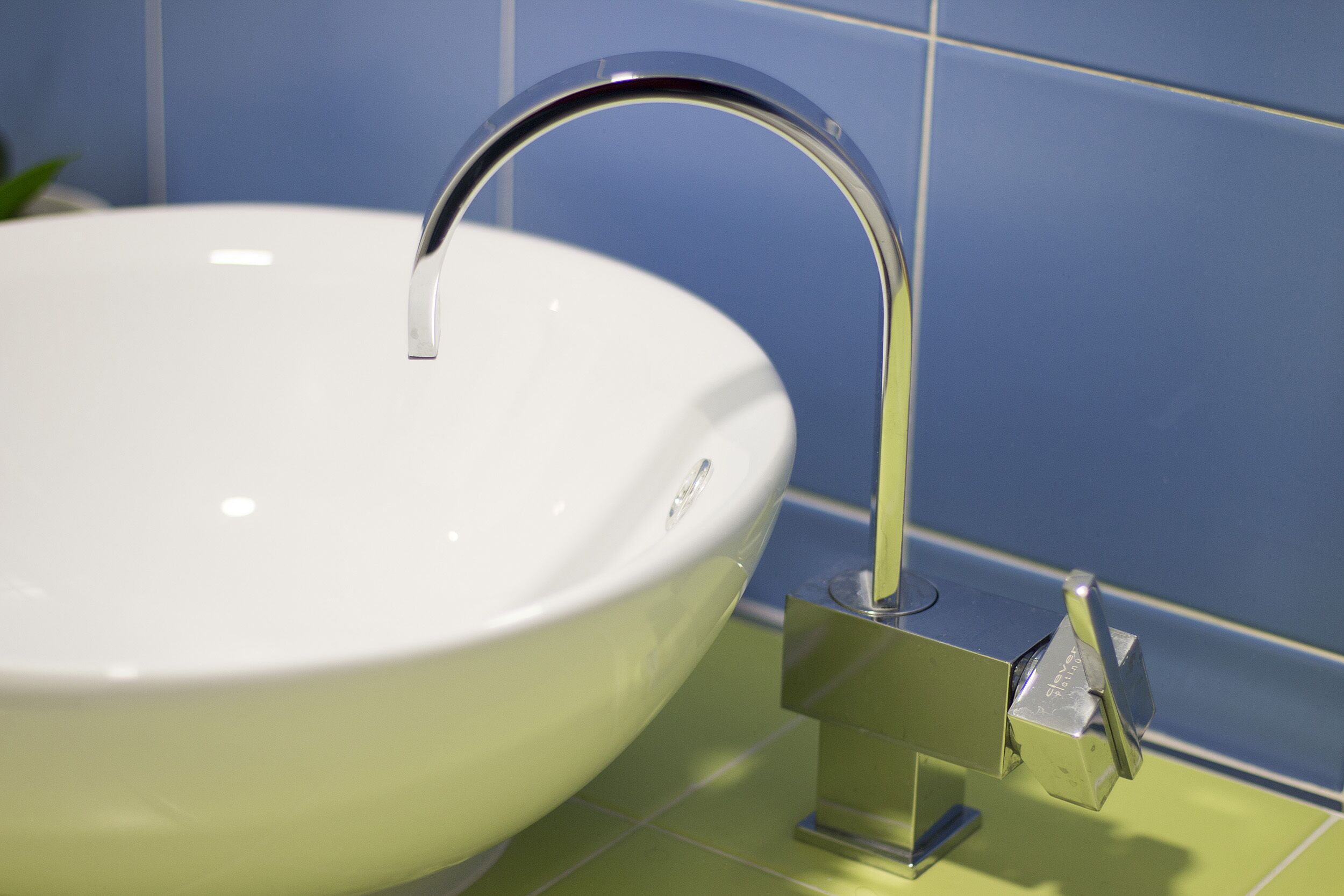 A white ceramic sink with a chrome faucet mounted on a green tile backsplash.