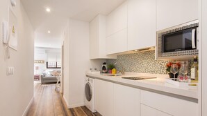 A modern kitchen with white cabinets, a built-in microwave, and a washing machine.