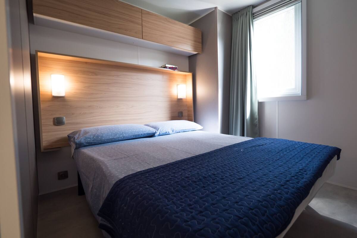 Un dormitorio moderno con cama, cabecero, lámparas de noche y ventana con cortinas.