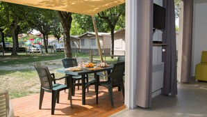 Un comedor con una mesa lista para dos personas, rodeada de sillas, y un sofá amarillo en la habitación contigua.