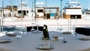 A table set for a meal with wine glasses and plates, overlooking a marina with boats. -  Hostal Bellavista Formentera (Formentera)