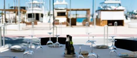A table set for a meal with wine glasses and plates, overlooking a marina with boats.