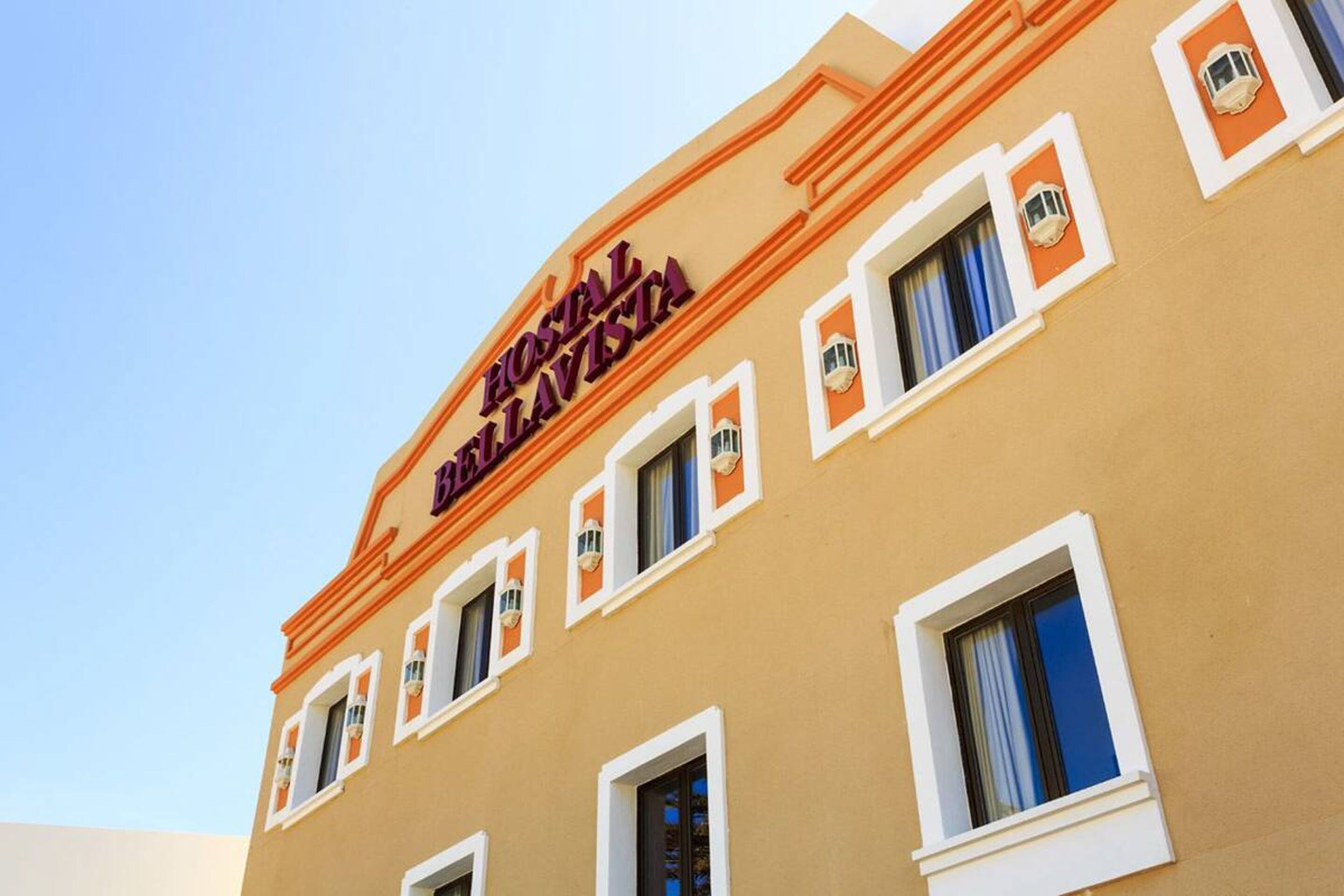 A hotel building with the sign "HOTEL BELAVISTA" and multiple windows with curtains.
