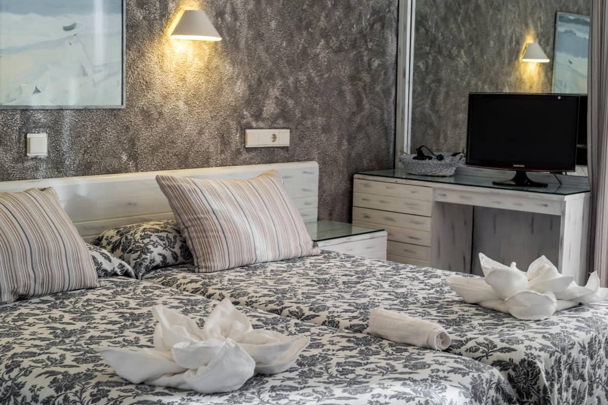 A modern bedroom with a large bed, two bedside lamps, a flat-screen TV, and a mirror.