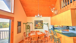 A wooden interior with a dining table, chairs, a kitchen area, and a deer mounted on the wall.