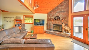 A living room with a stone fireplace, a television, a sofa, and a deer head sculpture.