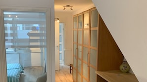 Een modern interieur met een houten vloer, een stoel, een kast met lades en uitzicht op een andere kamer met een bed.