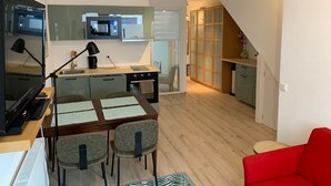 Een ruimtelijk ingedeelde leefruimte met een kitchenette, een eethoek en een rode bank.