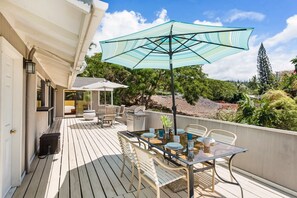A covered outdoor patio with a table set for dining, surrounded by chairs and a large umbrella.