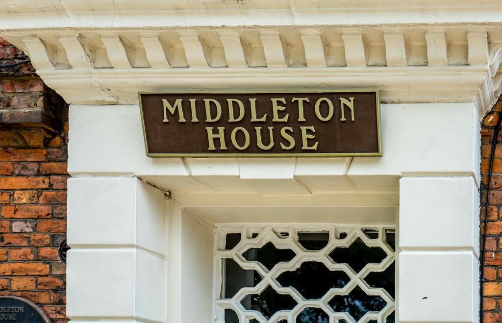 Un cartel con la inscripción 'Middleton House' sobre una puerta blanca con un ventanal de celosía decorativa.
