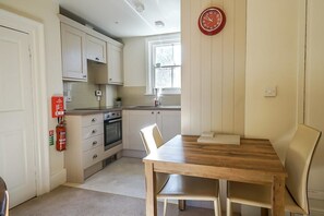 A compact kitchen with white cabinets, a wooden dining table, and a red clock on the wall.