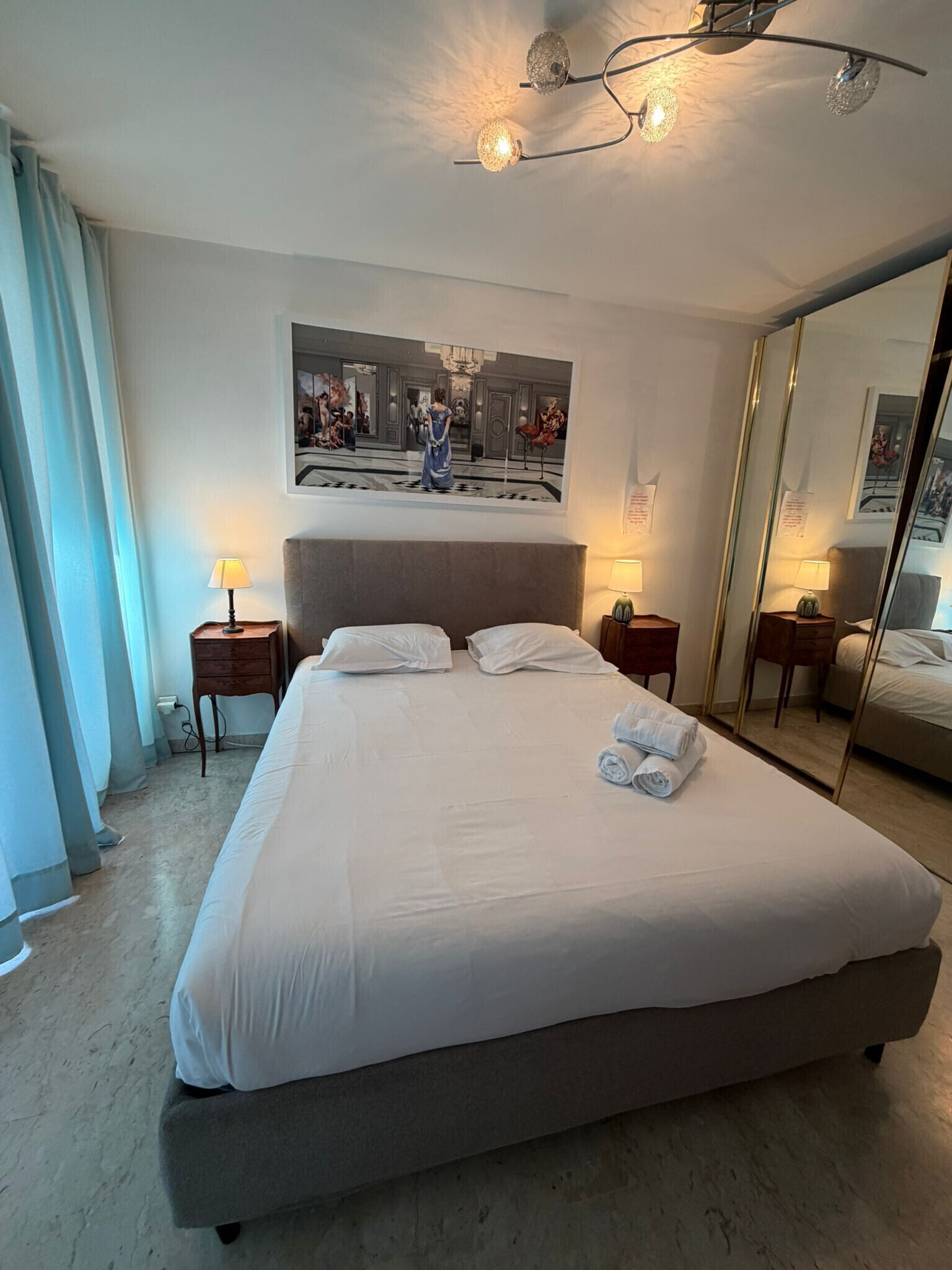 Una camera d'albergo con un letto grande, due comodini con lampade, un ampio specchio e un quadro appeso al muro.