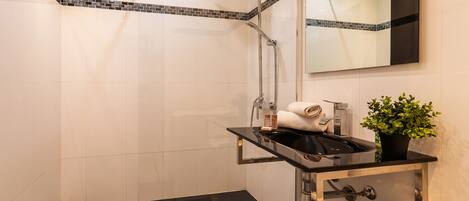 A modern bathroom with a glass shower enclosure, a black countertop sink, a mirror, and a potted plant.