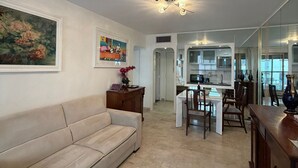 Un salon avec un canapé, un coin repas avec des chaises, une cuisine avec des placards et un grand miroir qui reflète la pièce.