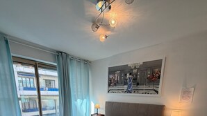 Une chambre d’hôtel avec un grand lit, un luminaire au plafond, un tableau encadré au mur et une vue sur l’extérieur.