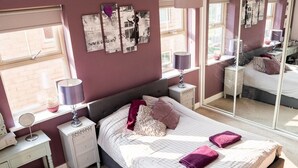 A bedroom with a large bed, bedside tables, a mirror, and a window with a view. - Modern Canalside City Townhouse - Parking & Garden (Leeds)