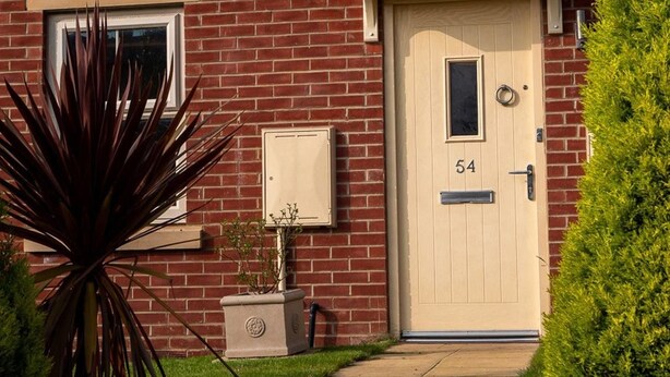 A brick house with a beige front door, a mailbox, and a small potted plant. - Modern Canalside City Townhouse - Parking & Garden (Leeds)