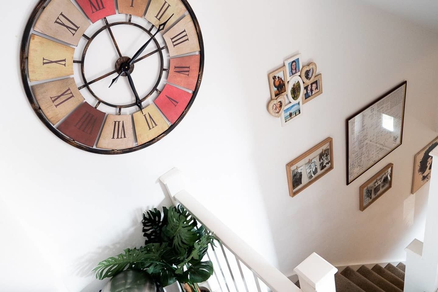 A wall with a large clock, framed photos, and a staircase.