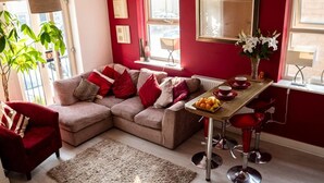 A cozy living room with a sectional sofa, red accents, and a dining area with red chairs. - Modern Canalside City Townhouse - Parking & Garden (Leeds)