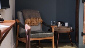 A cozy room with a grey armchair, a small wooden table with a kettle, and a coffee machine. - Castle Inn (Wareham)