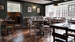 A restaurant with multiple tables and chairs, framed artwork on the walls, and large windows allowing natural light. - Castle Inn (Wareham)