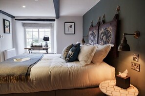 A bedroom with a bed, a bedside table, a lamp, a window, and a wall-mounted shelf. - Castle Inn (Wareham)