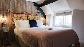 Un dormitorio con cabecera de madera, cama con ropa de cama blanca y rosa, mesita de noche con lámpara y ventana con luz natural.