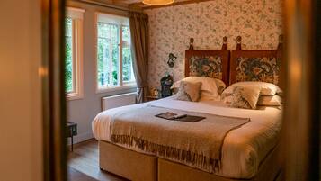 Une chambre avec un grand lit, une fenêtre avec des rideaux, un radiateur et un mur recouvert d’un papier peint à motifs floraux.