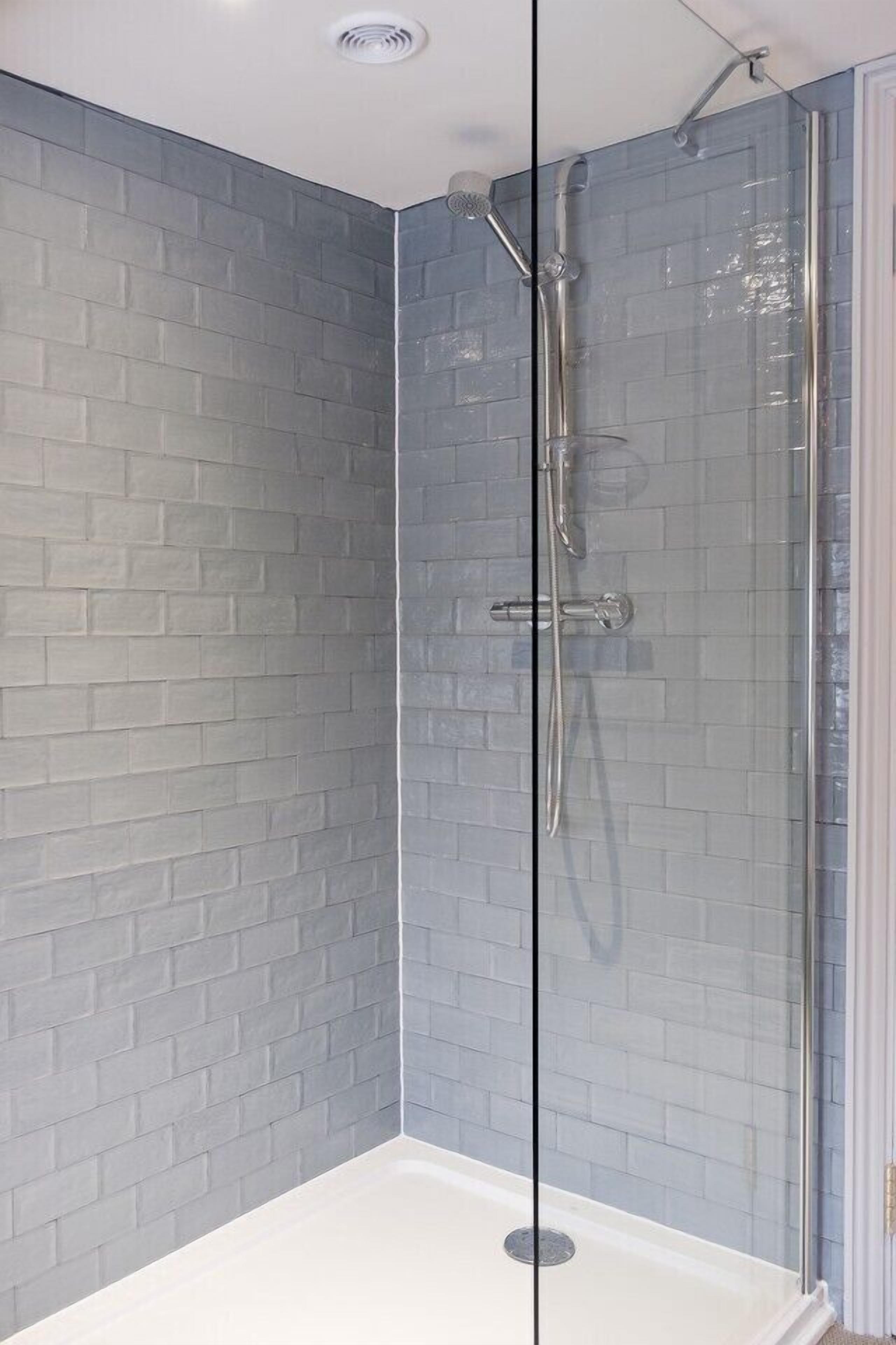 A glass-enclosed shower with a white floor, grey brick-patterned walls, and a white ceiling.