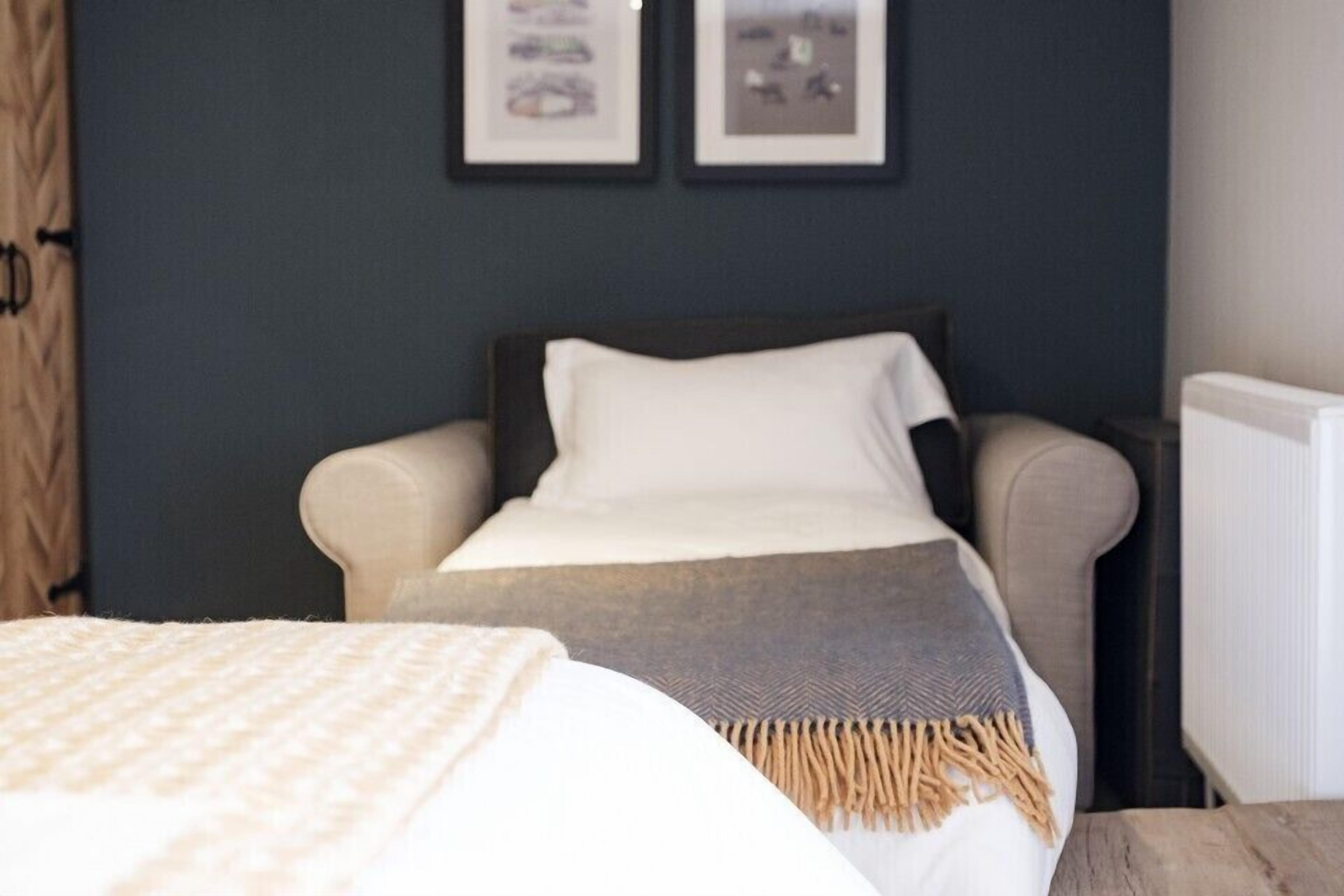 A bedroom with a bed, a chair, and a nightstand. There are two framed pictures on the wall.