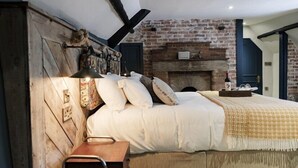A bedroom with a brick fireplace, a wooden headboard, and a bedside table with a lamp. - Castle Inn (Wareham)