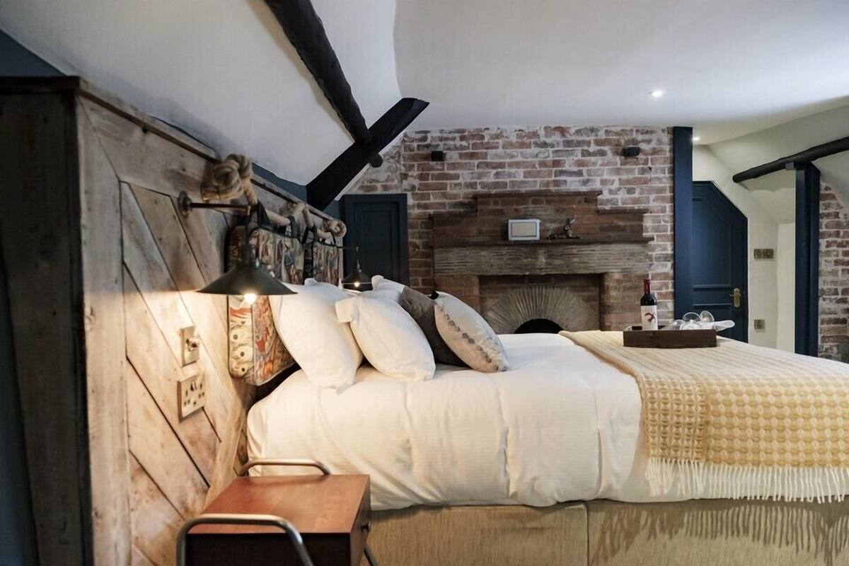 Une chambre avec une cheminée en briques, une tête de lit en bois et une table de chevet avec une lampe.