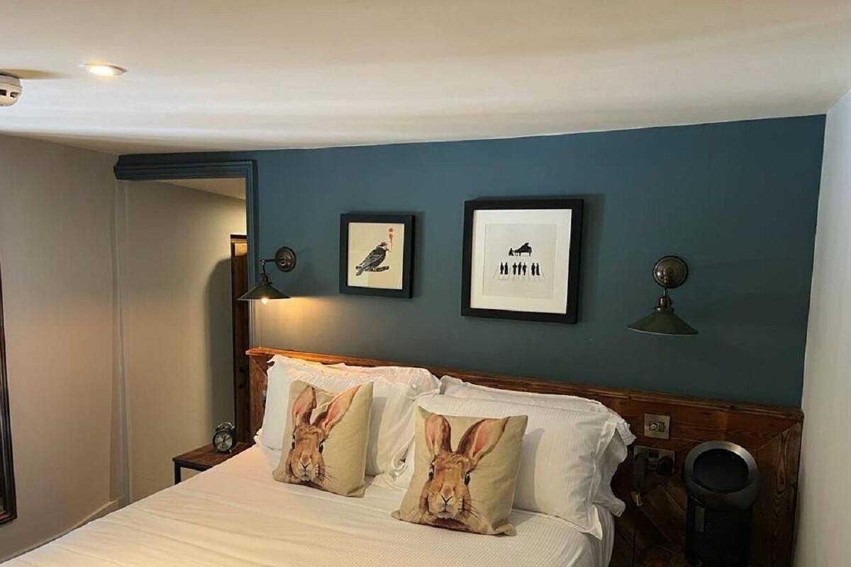Une chambre d’hôtel avec un lit, deux oreillers ornés de motifs représentant des lapins, un tableau encadré accroché au mur, une petite table avec une lampe et une poubelle.