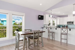 A modern kitchen with white cabinets, a wooden dining table, and a balcony with a view of houses. - Steps To Beach | Private Pool | Pet-Friendly (Port Saint Joe)