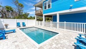 Un giardino sul retro con piscina, poltrone Adirondack blu e un recinto bianco.