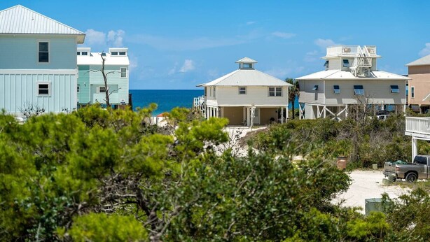 Una proprietà fronte spiaggia con diverse case, tra cui una casa azzurra e una beige con un balcone bianco.