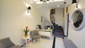 A modern living room with a white sofa, a striped armchair, a small side table with a plant, a white console table with a laptop, and a staircase with a decorative railing. - Violin Boutique Hotel (Istanbul)